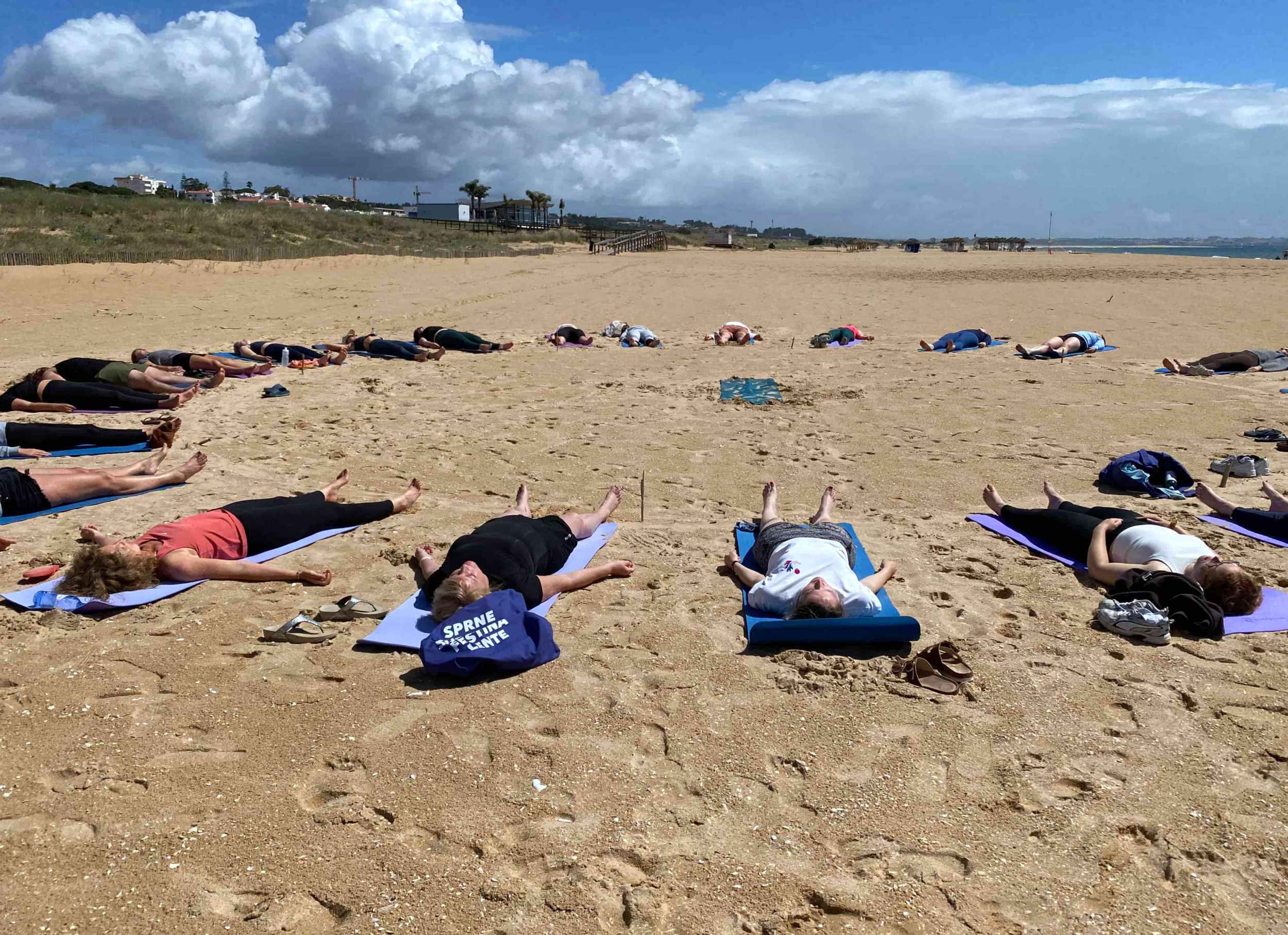 Private group yoga session on a beach in Lagos, Portugal with participants in enjoying relaxation in savasana pose facing the open sky.