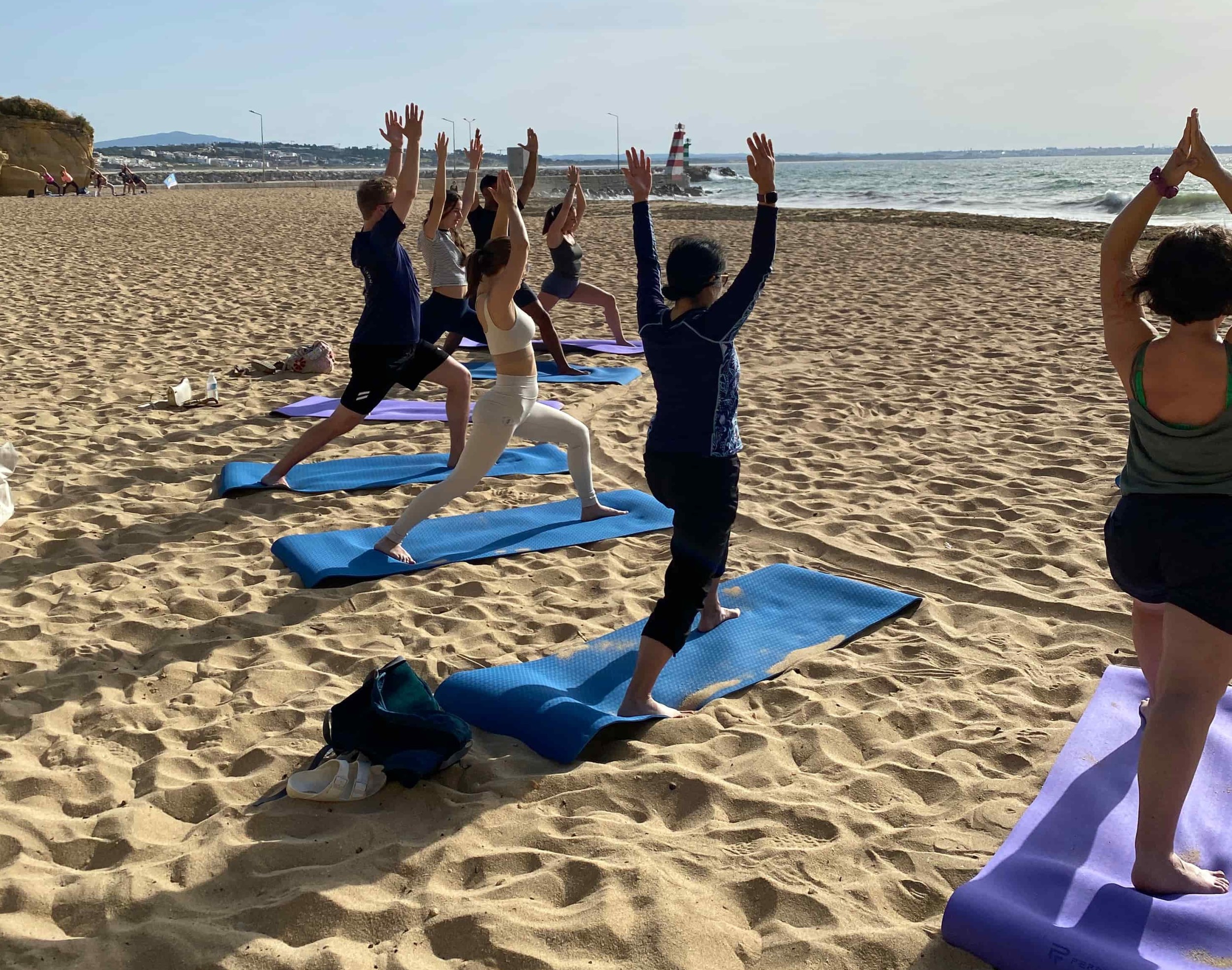 Private group yoga session on a beach in Lagos, Portugal with participants in warrior pose facing the ocean.