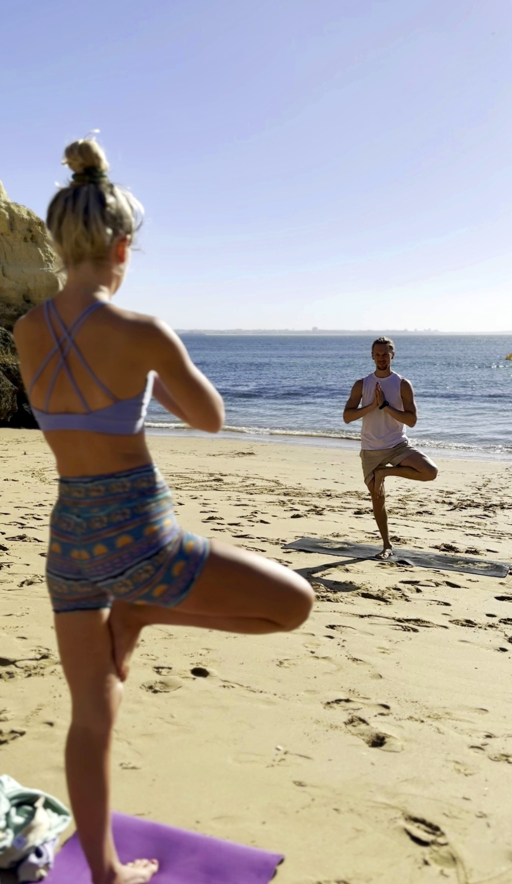 Private yoga class on a beach in Lagos, Algarve, with a yoga teacher and a student doing tree pose by the ocean.